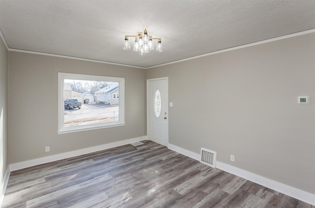 foyer with baseboards, ornamental molding, visible vents, a chandelier, and wood finished floors