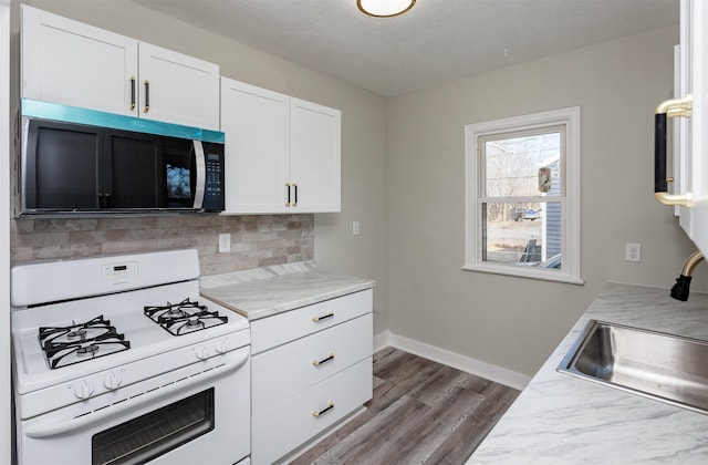 kitchen with white range with gas stovetop, white cabinets, backsplash, light countertops, and dark wood-style floors