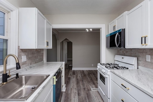 kitchen featuring a sink, tasteful backsplash, dishwashing machine, white gas range oven, and white cabinetry