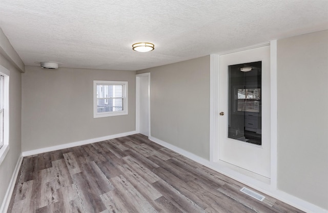 unfurnished room featuring baseboards, visible vents, a textured ceiling, and wood finished floors