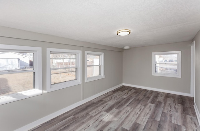 unfurnished room with a textured ceiling, wood finished floors, and baseboards