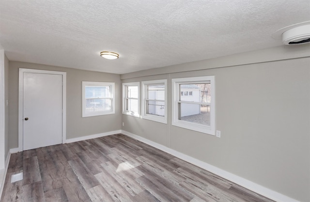 spare room featuring a textured ceiling, wood finished floors, and a healthy amount of sunlight