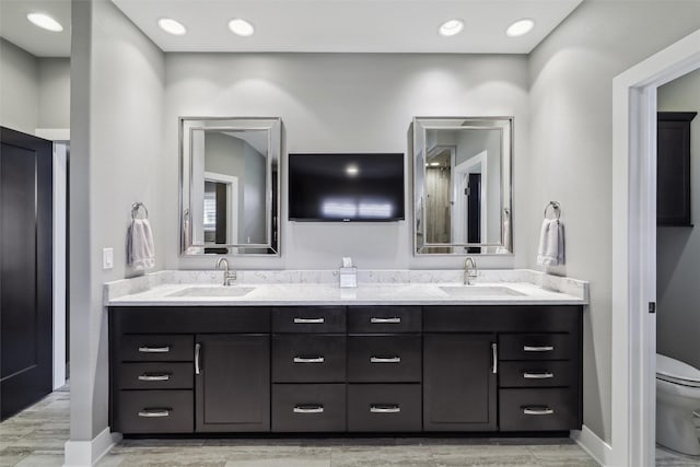bathroom with toilet, baseboards, double vanity, and a sink