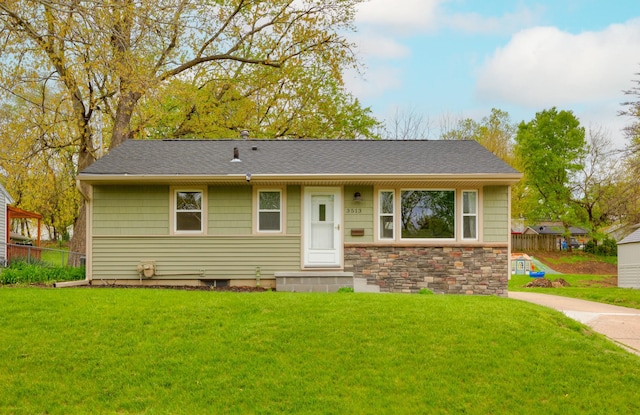 ranch-style house with entry steps, fence, stone siding, roof with shingles, and a front lawn