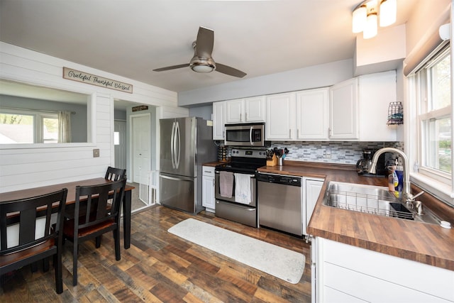 kitchen featuring wooden counters, a sink, stainless steel appliances, white cabinets, and backsplash