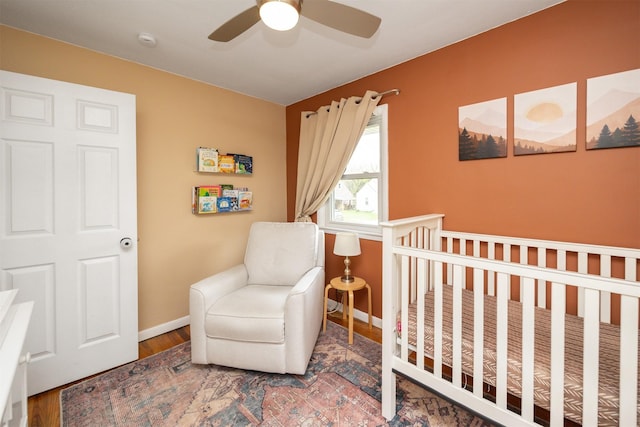 bedroom with baseboards, a ceiling fan, a crib, and wood finished floors