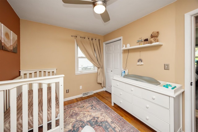 bedroom with a closet, wood finished floors, visible vents, ceiling fan, and baseboards