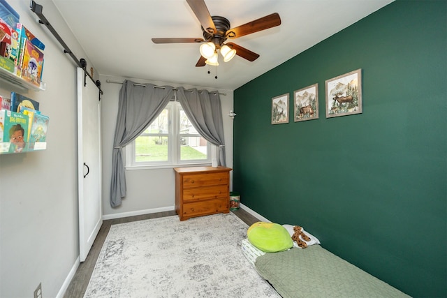 bedroom with ceiling fan, a barn door, baseboards, and wood finished floors