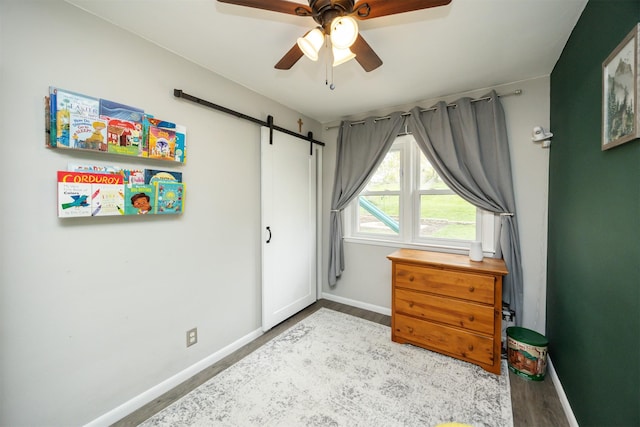 bedroom with a barn door, baseboards, a ceiling fan, and wood finished floors