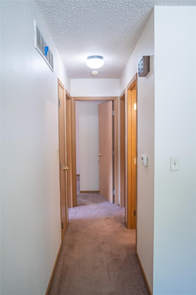 hallway featuring light colored carpet, a textured ceiling, and visible vents