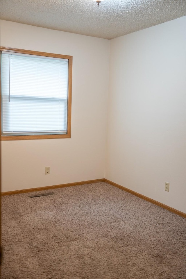 empty room with a textured ceiling, baseboards, visible vents, and carpet