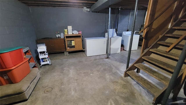 unfinished basement with stairs, fridge, concrete block wall, and washer and clothes dryer