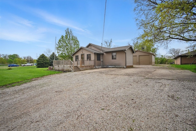 view of front of home with a detached garage, driveway, an outbuilding, a wooden deck, and a front lawn