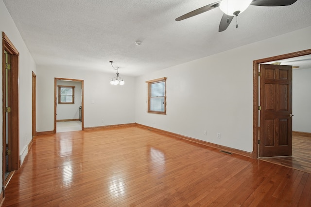 spare room featuring plenty of natural light, visible vents, light wood-style flooring, and ceiling fan with notable chandelier