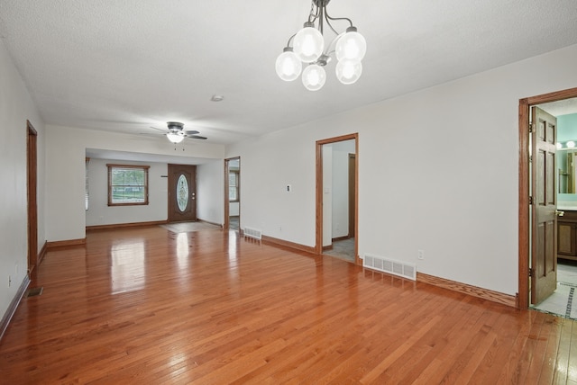 unfurnished living room with baseboards, light wood finished floors, visible vents, and ceiling fan with notable chandelier