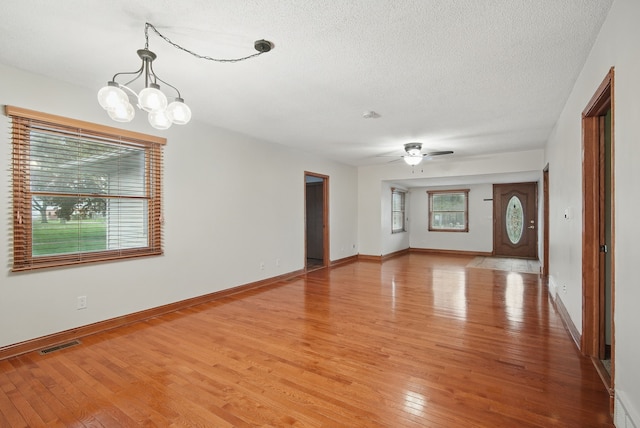 empty room with ceiling fan with notable chandelier, light wood-type flooring, visible vents, baseboards, and a textured ceiling