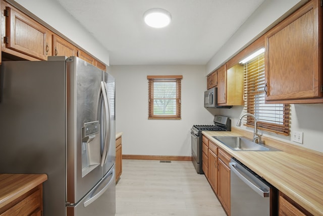 kitchen with a sink, light wood-type flooring, baseboards, light countertops, and appliances with stainless steel finishes