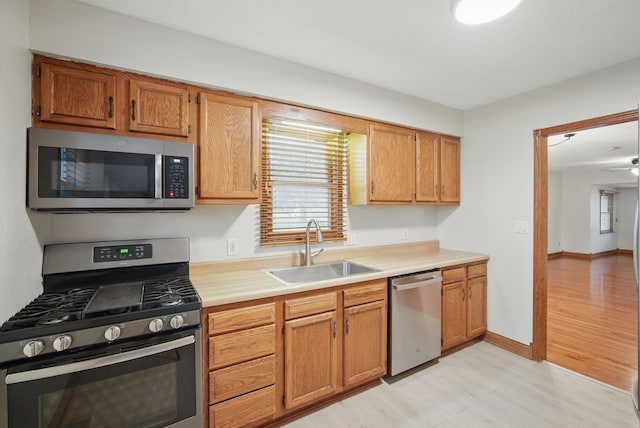 kitchen with stainless steel appliances, brown cabinetry, a sink, light countertops, and light wood-type flooring