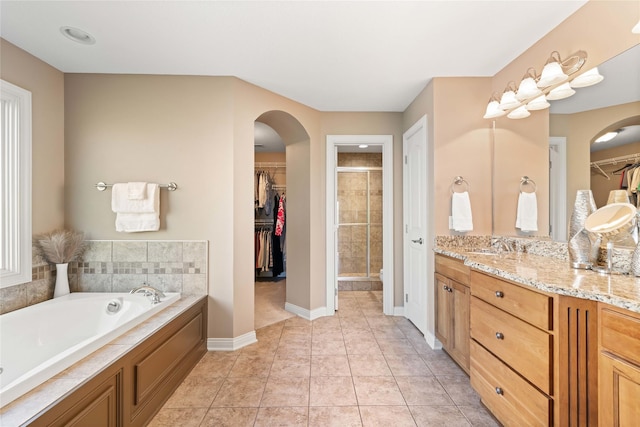 bathroom featuring vanity, baseboards, a shower stall, a walk in closet, and a garden tub