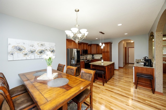 4110 140th St, Urbandale, IA 50323 - dining space featuring arched walkways, light wood finished floors, an inviting chandelier, and recessed lighting
