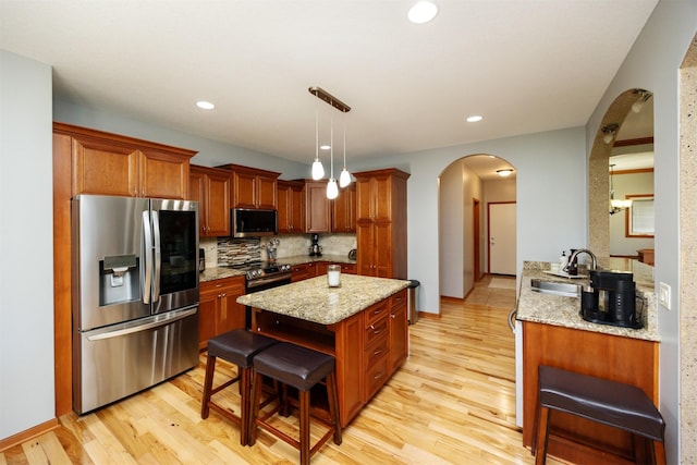 4110 140th St, Urbandale, IA 50323 - kitchen featuring light wood finished floors, a sink, arched walkways, tasteful backsplash, and appliances with stainless steel finishes