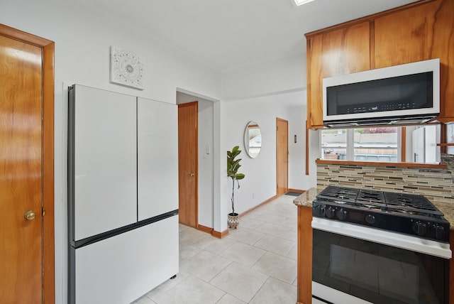 kitchen with brown cabinetry, baseboards, white appliances, decorative backsplash, and light tile patterned flooring