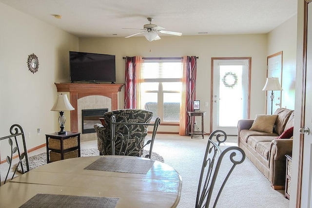 living area featuring light colored carpet, a tile fireplace, ceiling fan, and plenty of natural light
