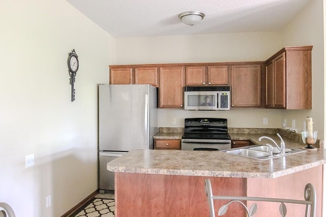 kitchen featuring a sink, a peninsula, brown cabinetry, light countertops, and appliances with stainless steel finishes