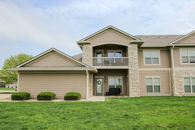 exterior space with roof with shingles, a front yard, stone siding, and a balcony