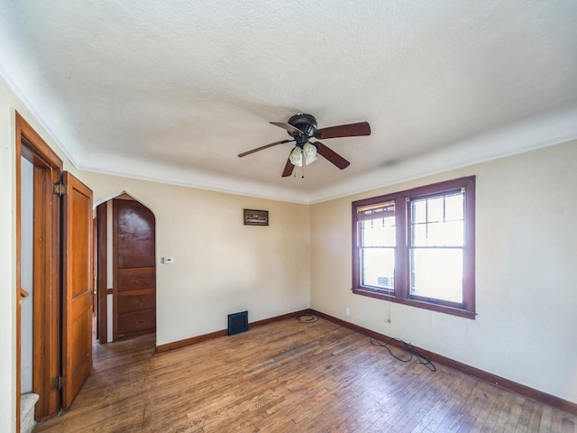 unfurnished room with hardwood / wood-style flooring, a textured ceiling, visible vents, ceiling fan, and baseboards