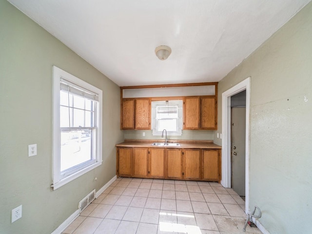 kitchen featuring brown cabinetry, light tile patterned flooring, visible vents, a sink, and light countertops