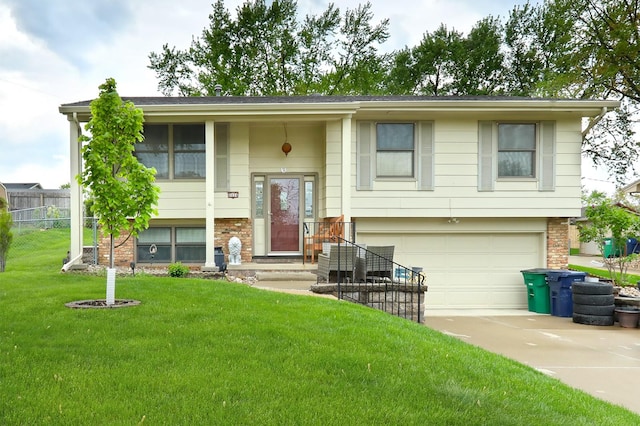 bi-level home featuring a garage, fence, a front lawn, brick siding, and driveway
