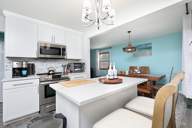 kitchen with stainless steel appliances, backsplash, light countertops, white cabinets, and a notable chandelier