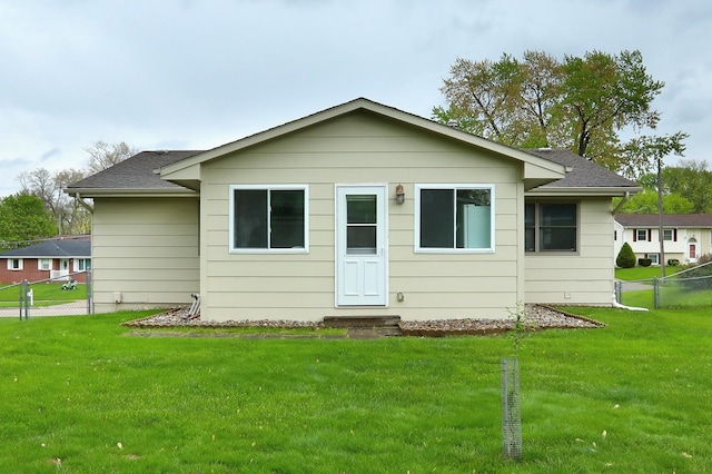 rear view of property featuring a yard, roof with shingles, and fence