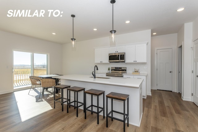 935 11th St, Waukee, IA 50263 - kitchen with appliances with stainless steel finishes, decorative backsplash, white cabinets, light wood finished floors, and recessed lighting