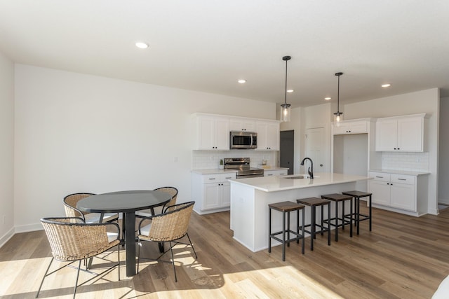 935 11th St, Waukee, IA 50263 - kitchen with appliances with stainless steel finishes, backsplash, a kitchen island with sink, light wood-type flooring, and recessed lighting