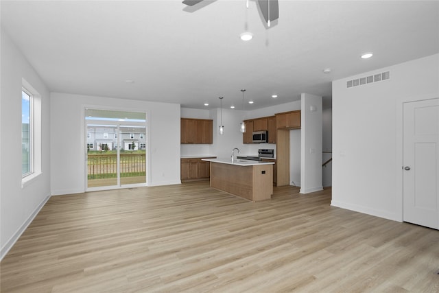 955 11th St, Waukee, IA 50263 - kitchen featuring stainless steel microwave, open floor plan, brown cabinets, light countertops, and recessed lighting