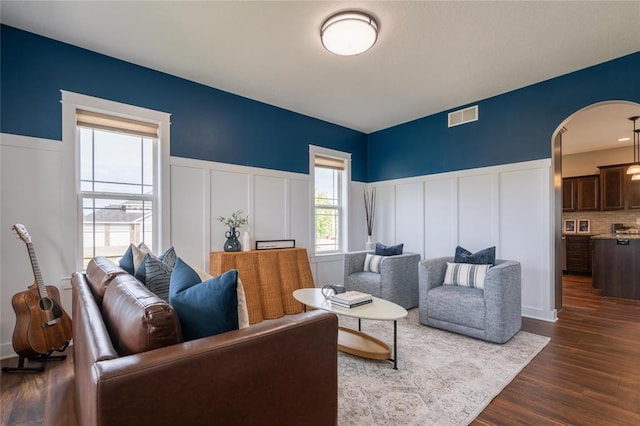 living room with a wainscoted wall, a decorative wall, dark wood-style floors, and visible vents