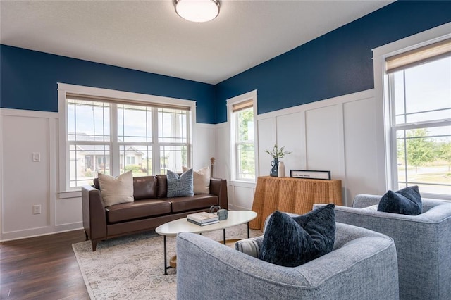 living room featuring dark wood-style flooring, a wealth of natural light, a decorative wall, and a wainscoted wall