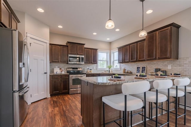 kitchen featuring dark brown cabinets, dark wood-style flooring, light stone countertops, appliances with stainless steel finishes, and decorative backsplash