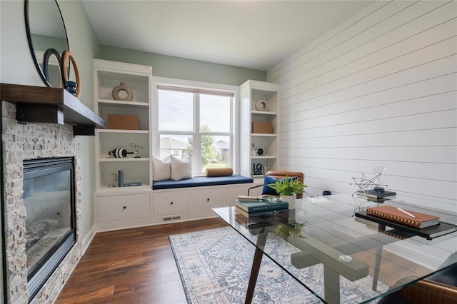 office area with a stone fireplace, wooden walls, dark wood finished floors, and visible vents