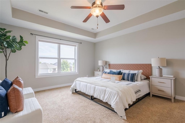 bedroom featuring a tray ceiling, baseboards, ceiling fan, visible vents, and light colored carpet