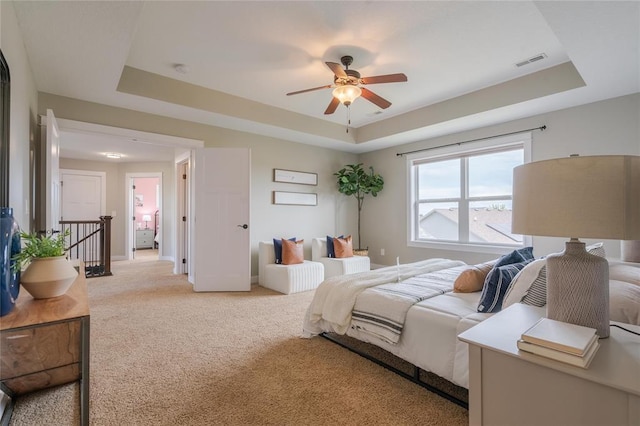 bedroom featuring a tray ceiling, ceiling fan, light carpet, and visible vents