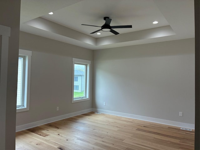 empty room featuring a tray ceiling, baseboards, ceiling fan, visible vents, and light wood-style floors