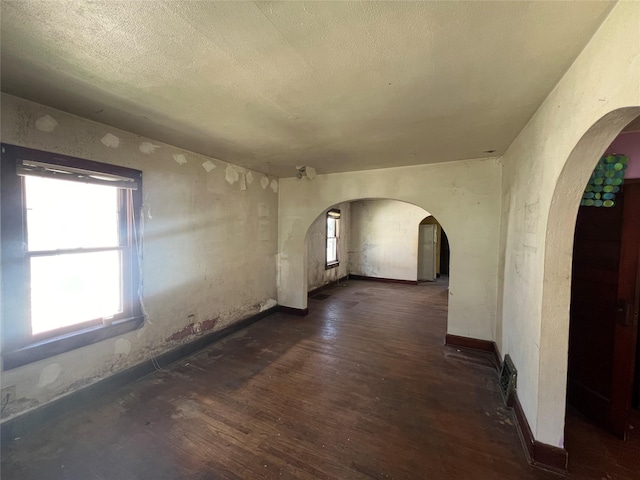 spare room with a textured ceiling, dark wood-type flooring, baseboards, and arched walkways