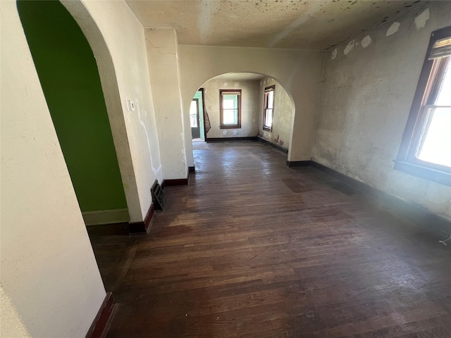 hall featuring arched walkways, baseboards, and wood finished floors
