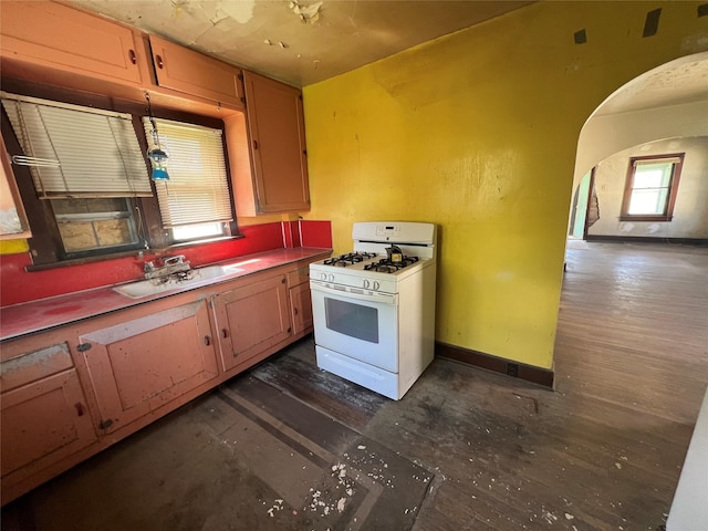 kitchen with a sink, baseboards, arched walkways, and white gas stove