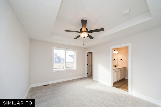 unfurnished bedroom featuring light colored carpet, visible vents, a tray ceiling, connected bathroom, and baseboards