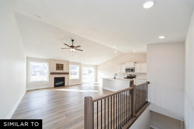 staircase with lofted ceiling, baseboards, ceiling fan, wood finished floors, and a fireplace