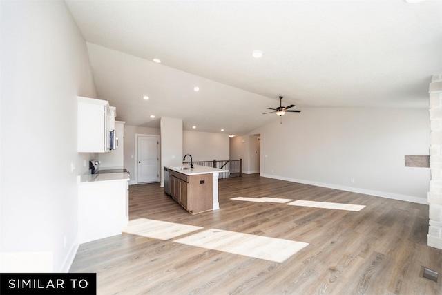 kitchen with lofted ceiling, ceiling fan, white cabinetry, open floor plan, and an island with sink